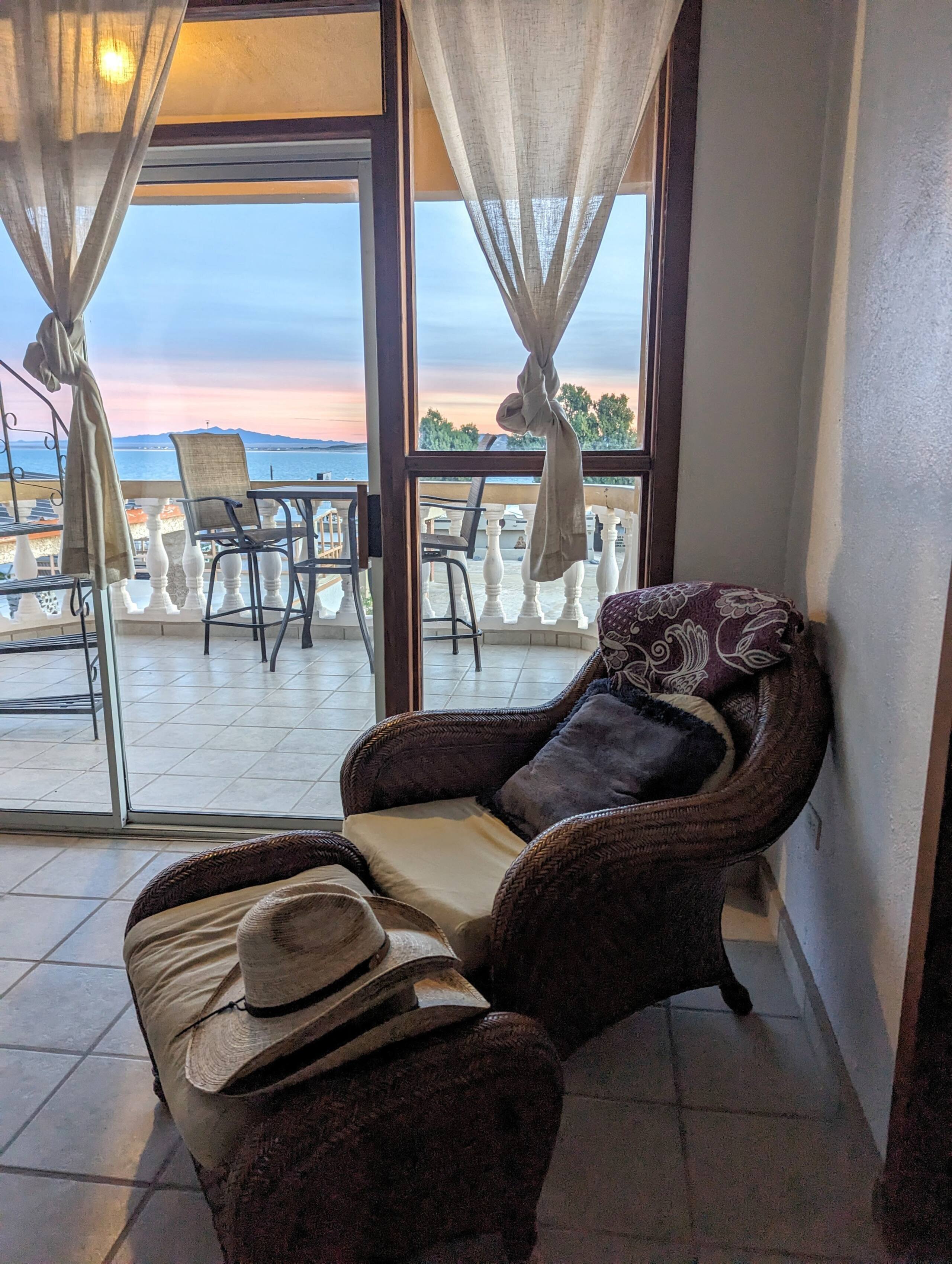 Wicker armchair and ottoman beside the balcony doors at Cholla Bay Vista with a view of the bay at dusk